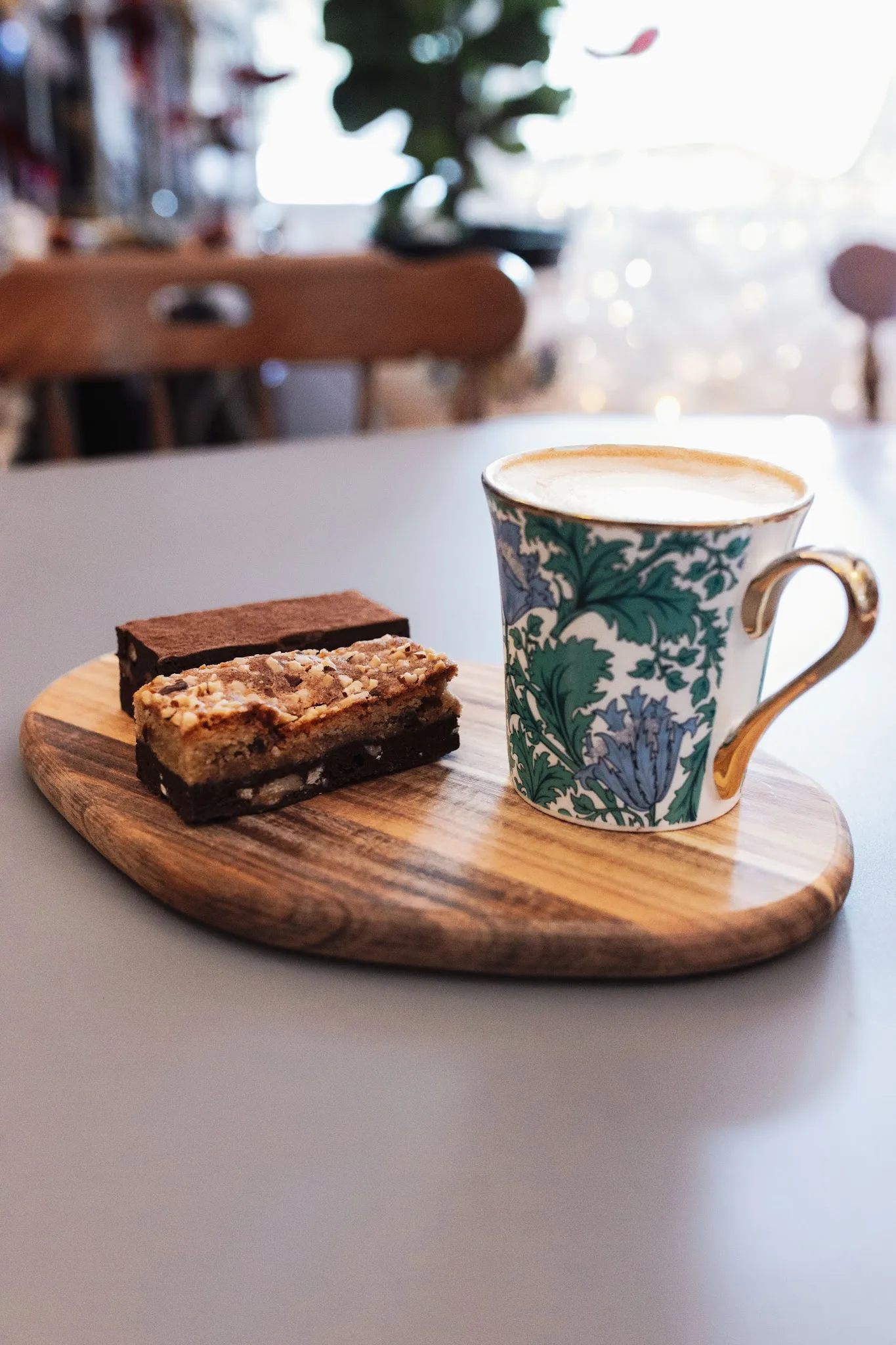 Flat white coffee in vintage floral mug with chocolate brownie and caramel slice on wooden board