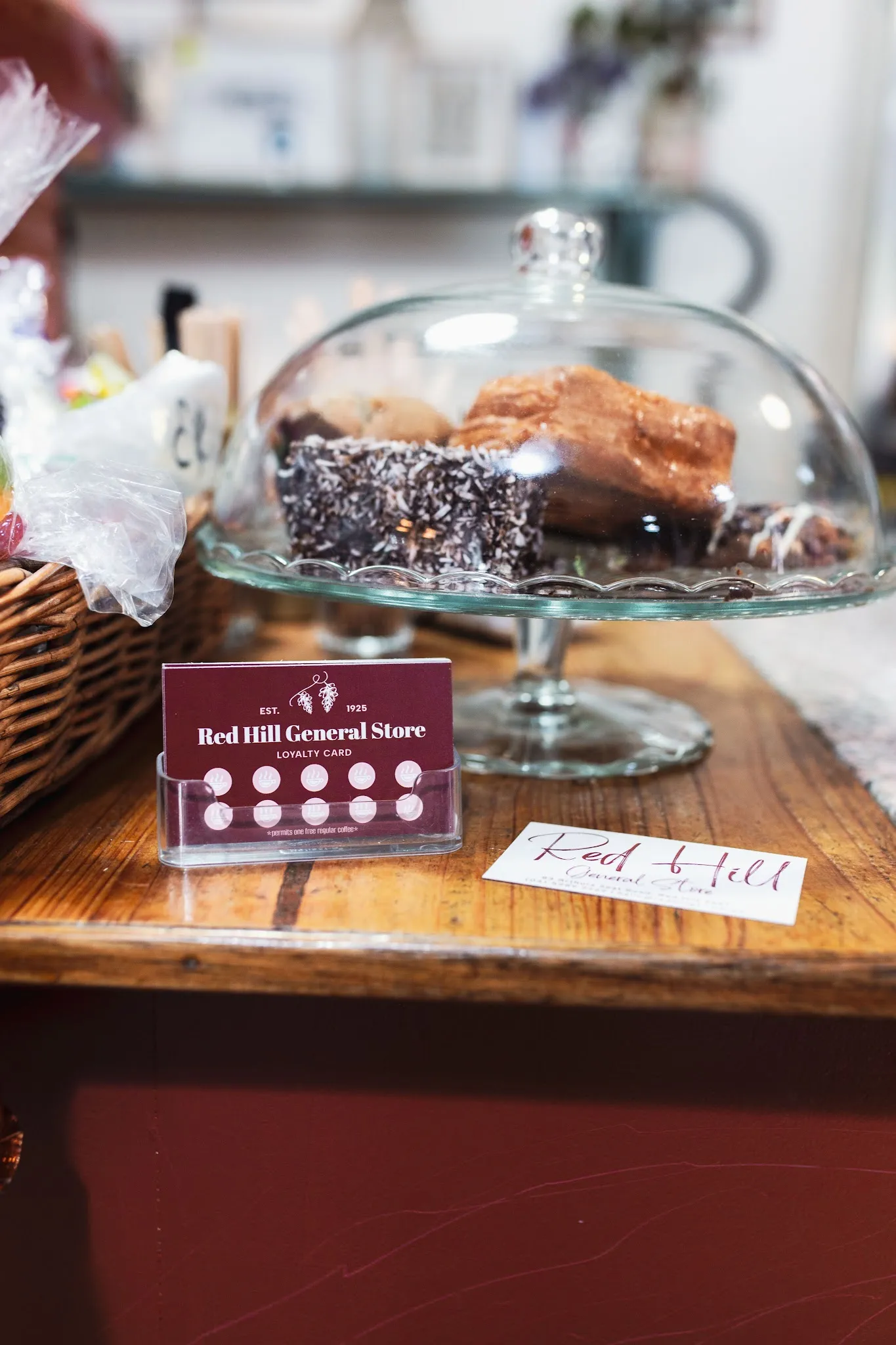 Red Hill General Store loyalty card and business card beside glass cake dome of baked goods on timber counter
