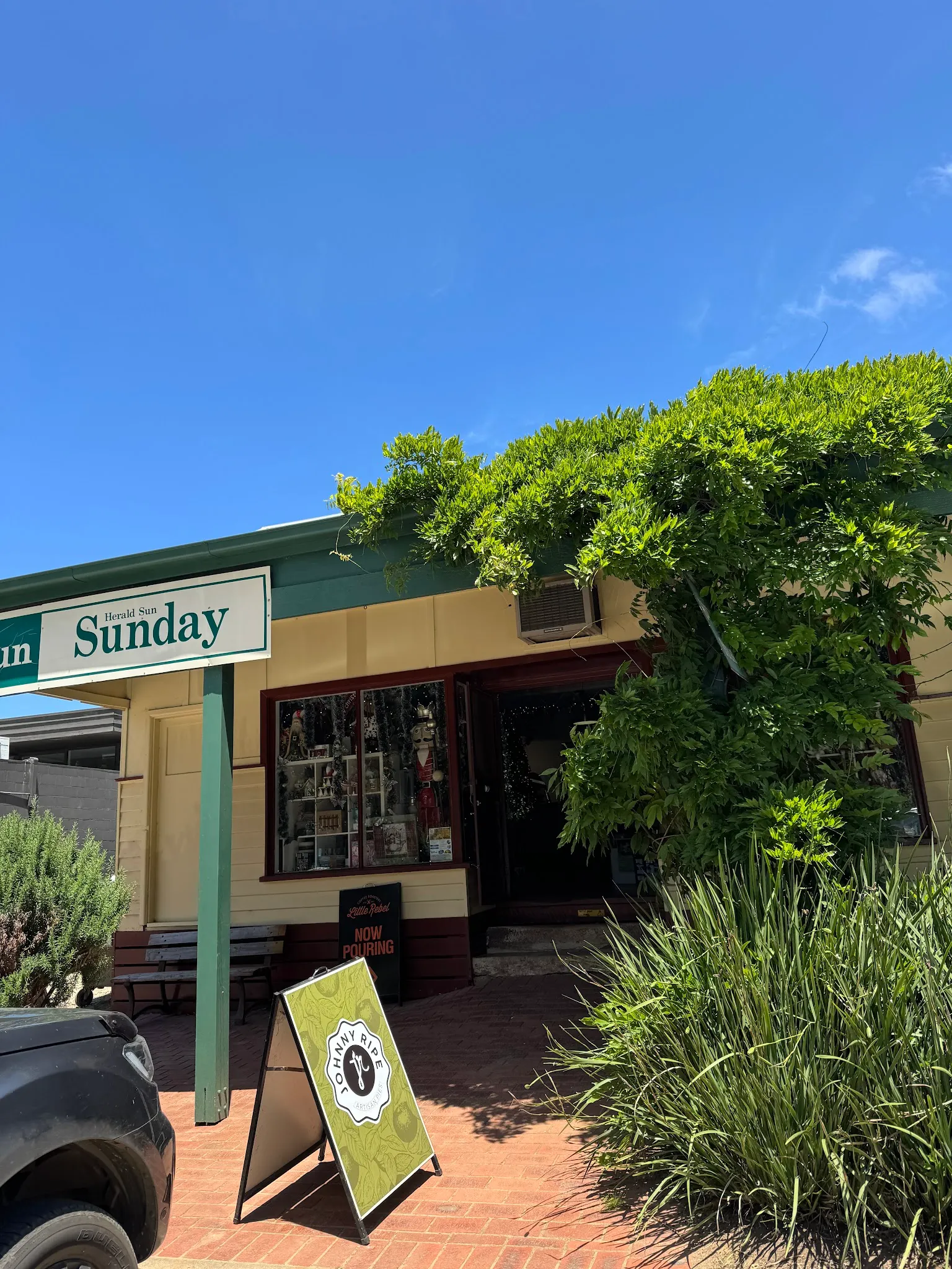 Red Hill General Store entrance with A-frame chalkboard, verandah posts, and climbing vine under blue sky