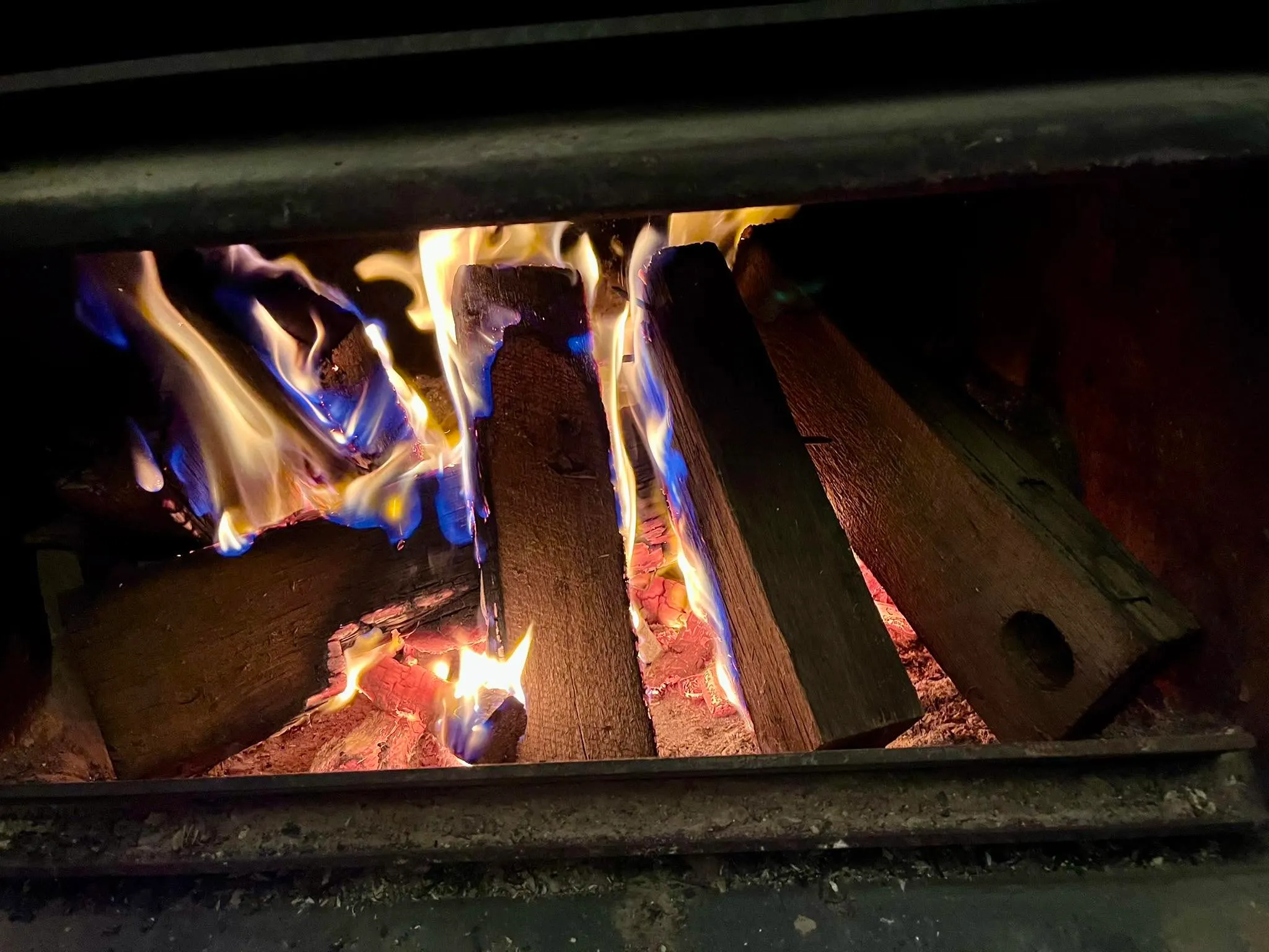 Close-up of wood fire with blue and yellow flames burning through a cast-iron firebox grate